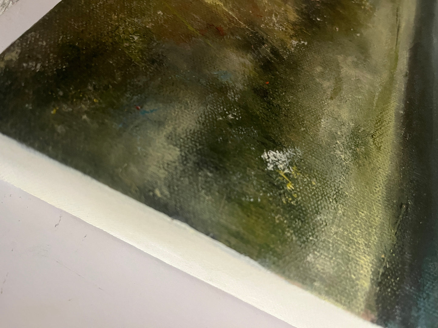 Close-up of a textured surface with greenish-brown coloration oil painting on boxed canvas of a meadow, grasses and flowers with mountains in the distance and a white, cloudy sky