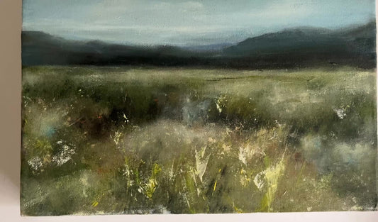 oil painting on boxed canvas of a meadow, grasses and flowers with mountains in the distance and a white, cloudy sky